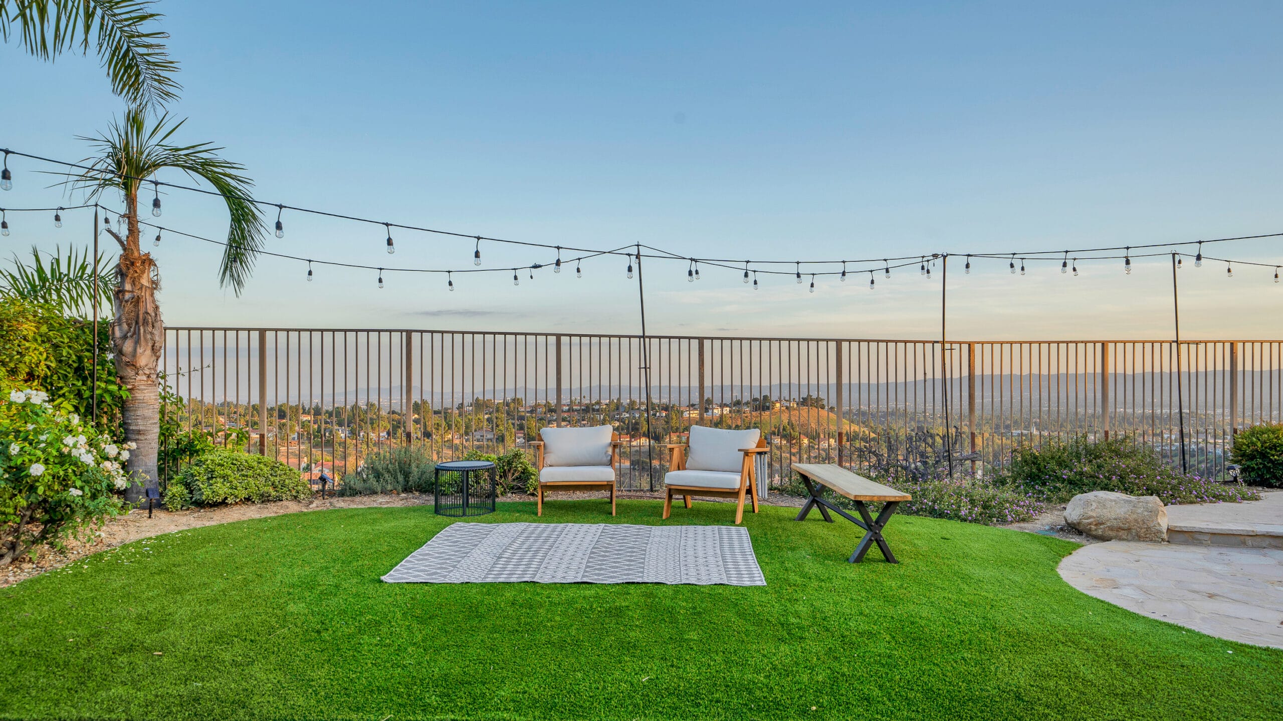 Porter Ranch hillside artificial turf install with string lights, lounge seating, and a panoramic LA basin view at sunset